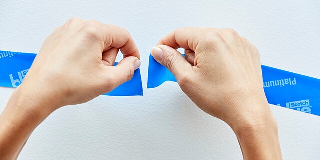 Une personne faisant chevaucher deux bandes de Ruban pour peintres pour lignes de démarcation ultra nettes Scotch®.
