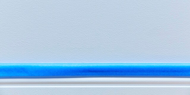 Ruban pour peintres bleu sur une plinthe blanche.
