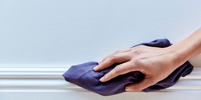 Une femme qui nettoie une plinthe avec un chiffon.
