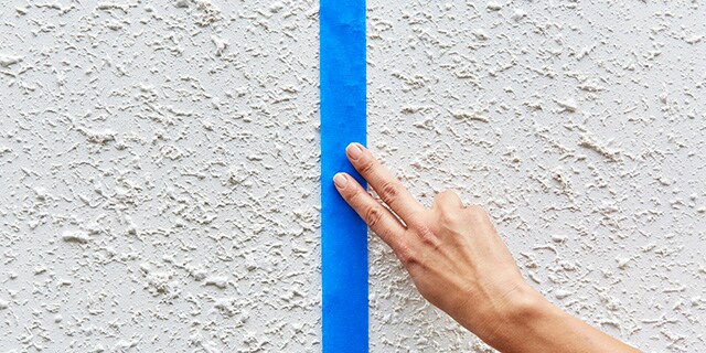 Une personne appliquant du ruban sur un mur texturé.
