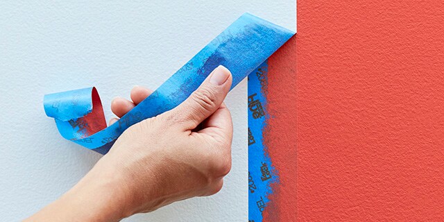 A hand removing ScotchBlue™ Painter's Tape from a painted wall.