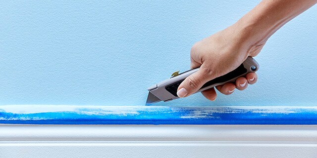 A person using a razor blade to score along the edge of painter's tape.
