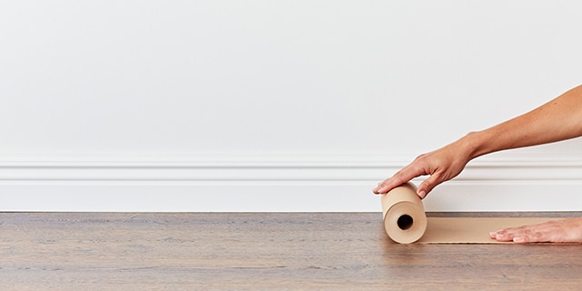 A person rolling rosin paper on a wooden floor along a wall.
